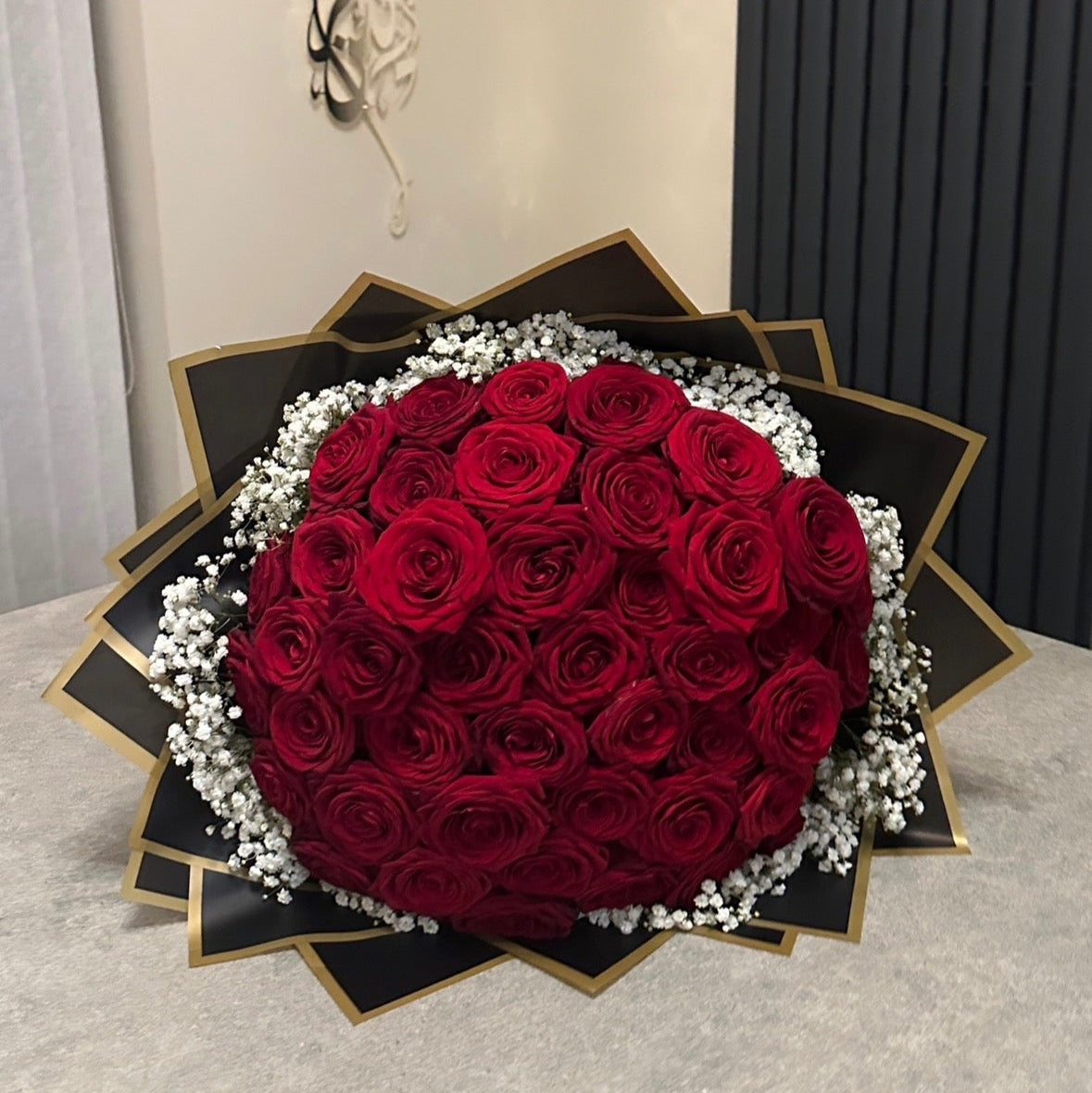 Bouquet of 50 red roses in velour black wrapping, with gypsophila surrounded, on a grey table.