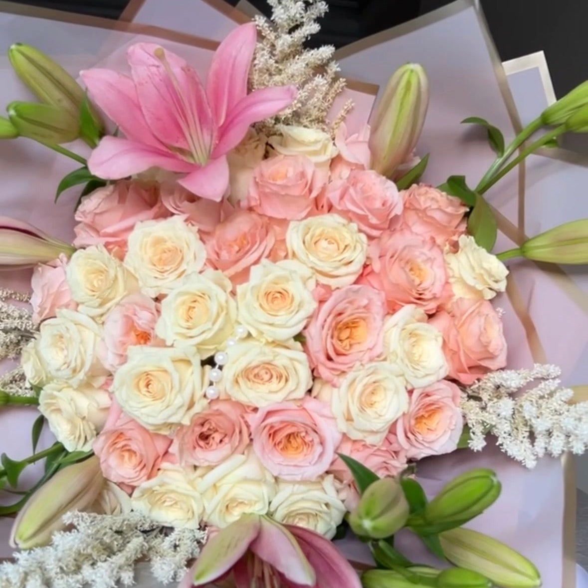 Bouquet of pink, white, and green flowers on a gray surface with stargazer lilies surrounding it.