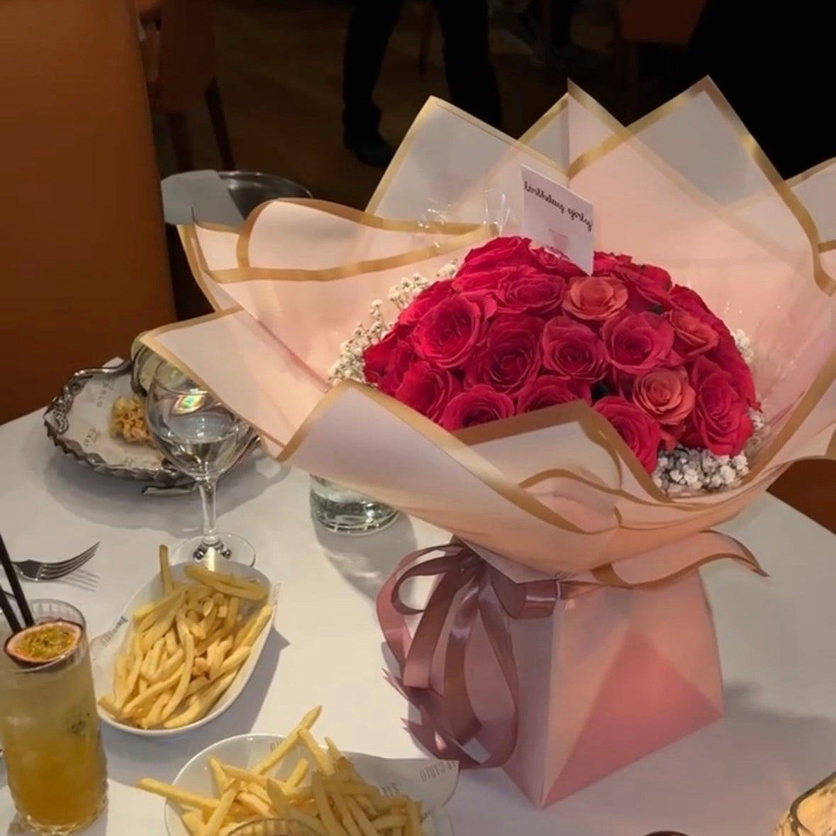 Bouquet of red roses on a table with food and drinks in a restaurant setting