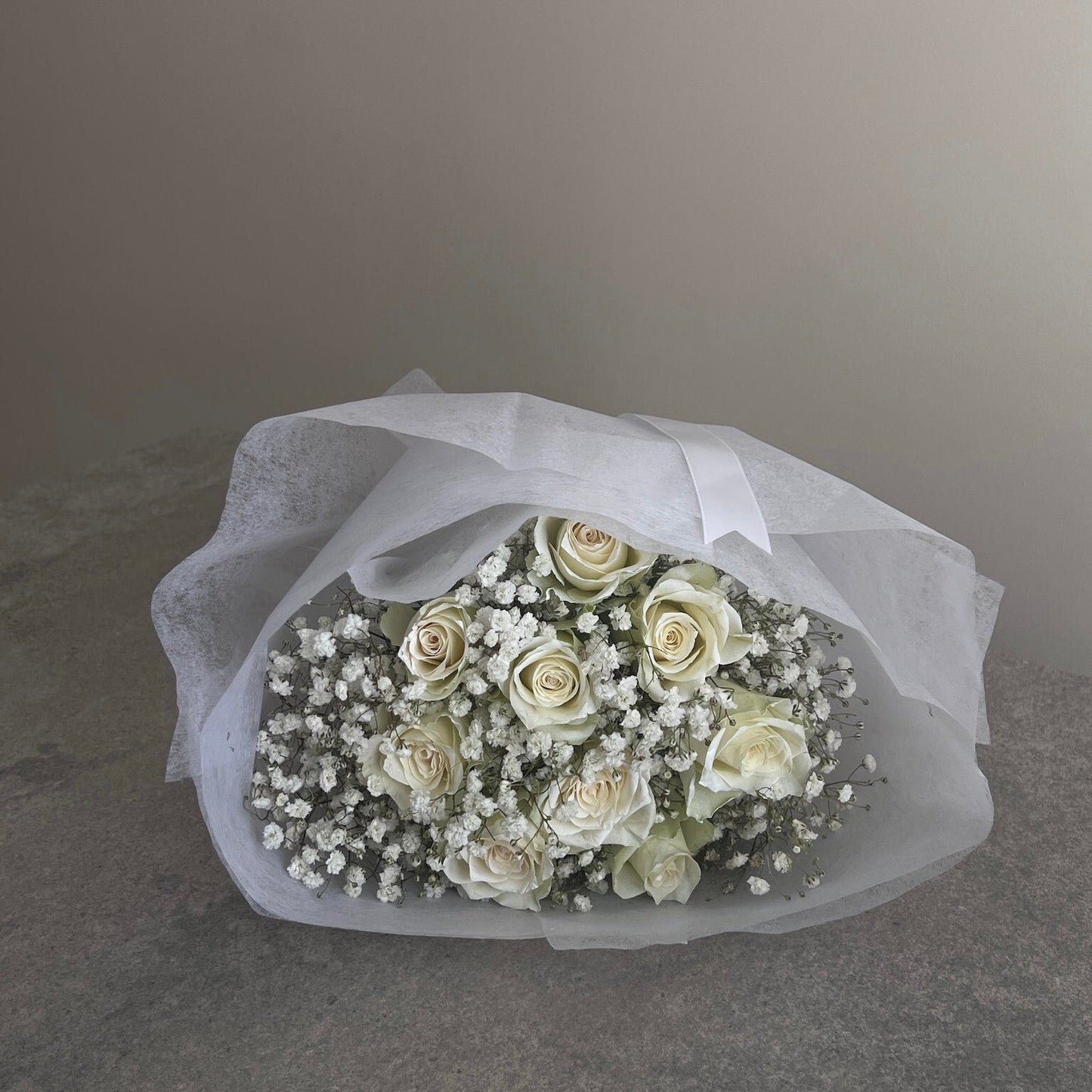 Bouquet of white flowers wrapped in white paper on a gray surface