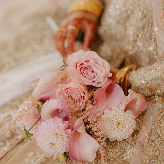Close-up of a bouquet of pink peonies, Dhalias, roses, held by a person in a bridal outfit.