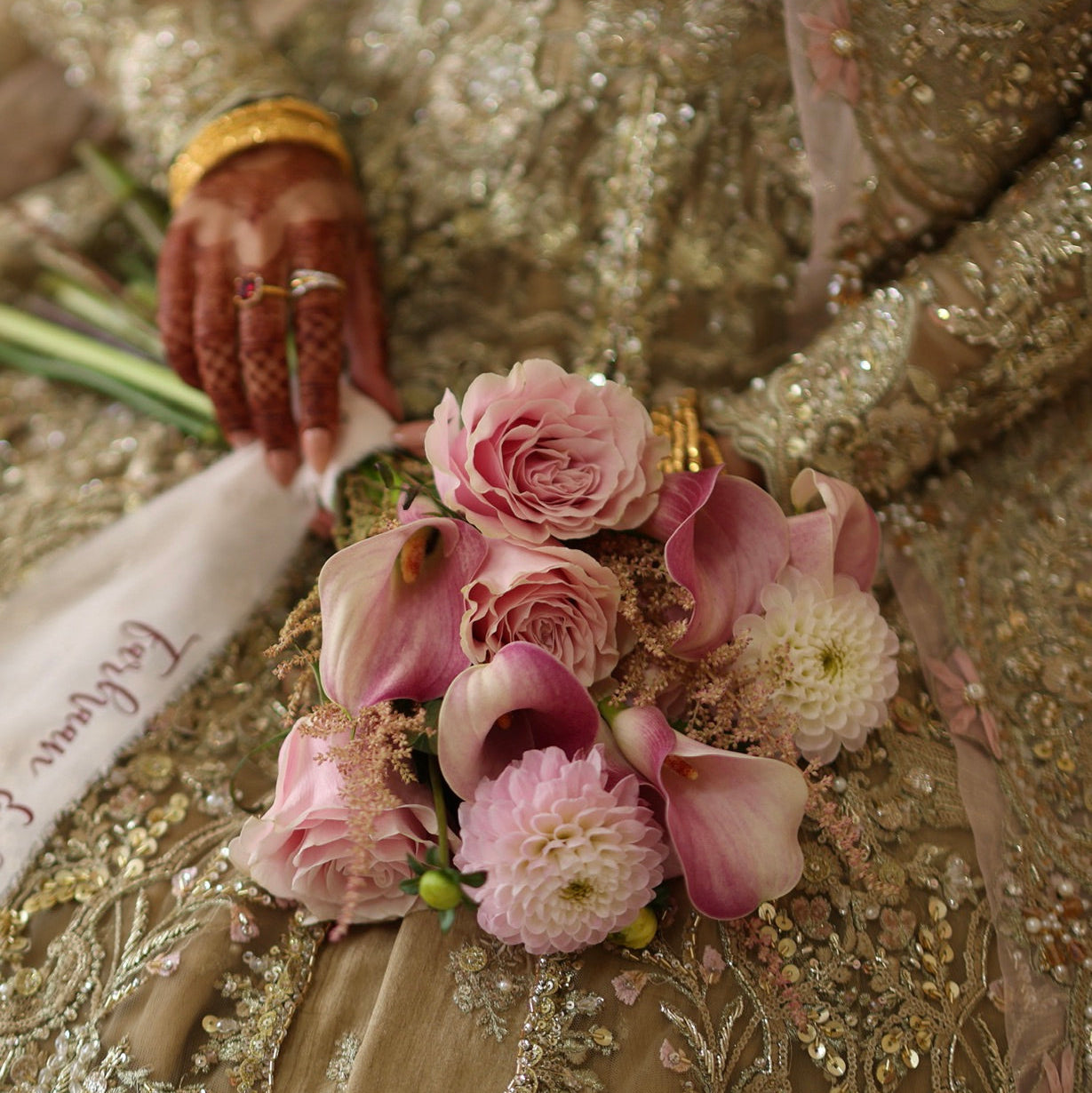 Close-up of a bouquet of pink peonies, Dhalias, roses, held by a person in a bridal outfit.