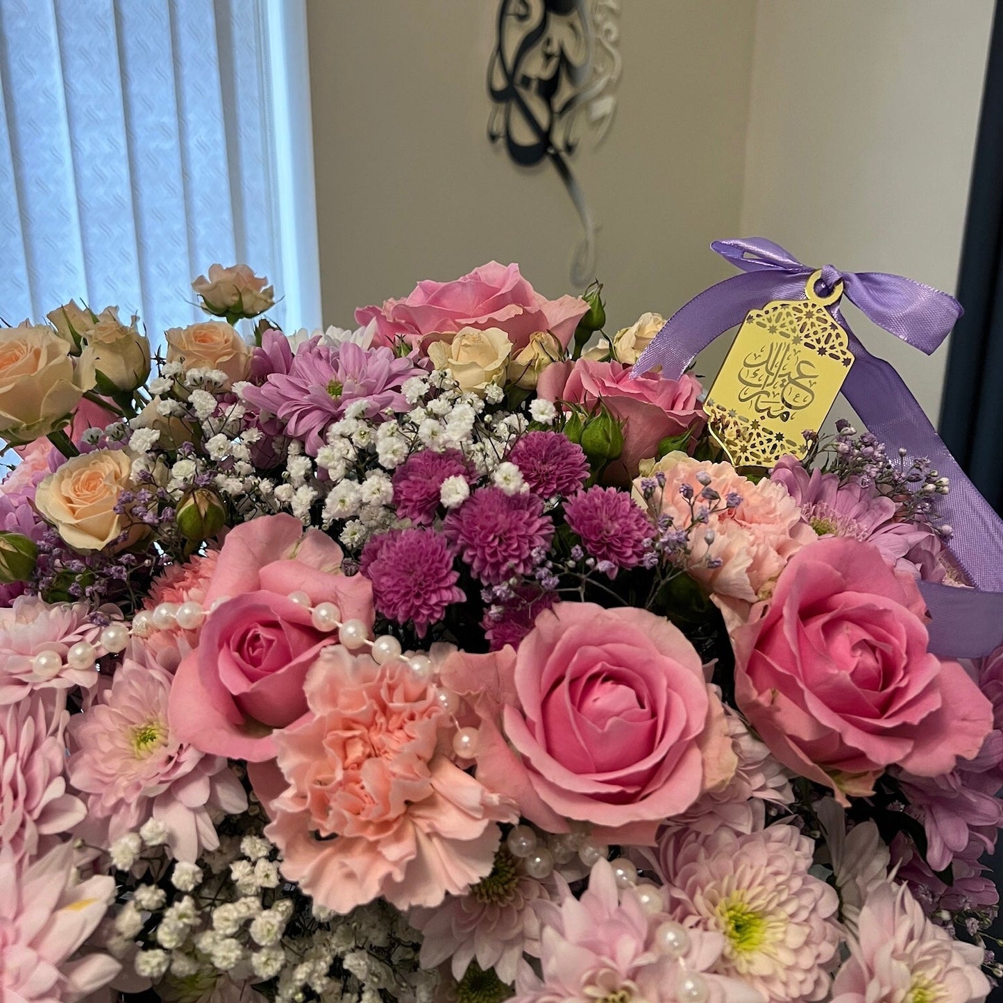 Bouquet of flowers with a purple ribbon and yellow tag in a room setting.