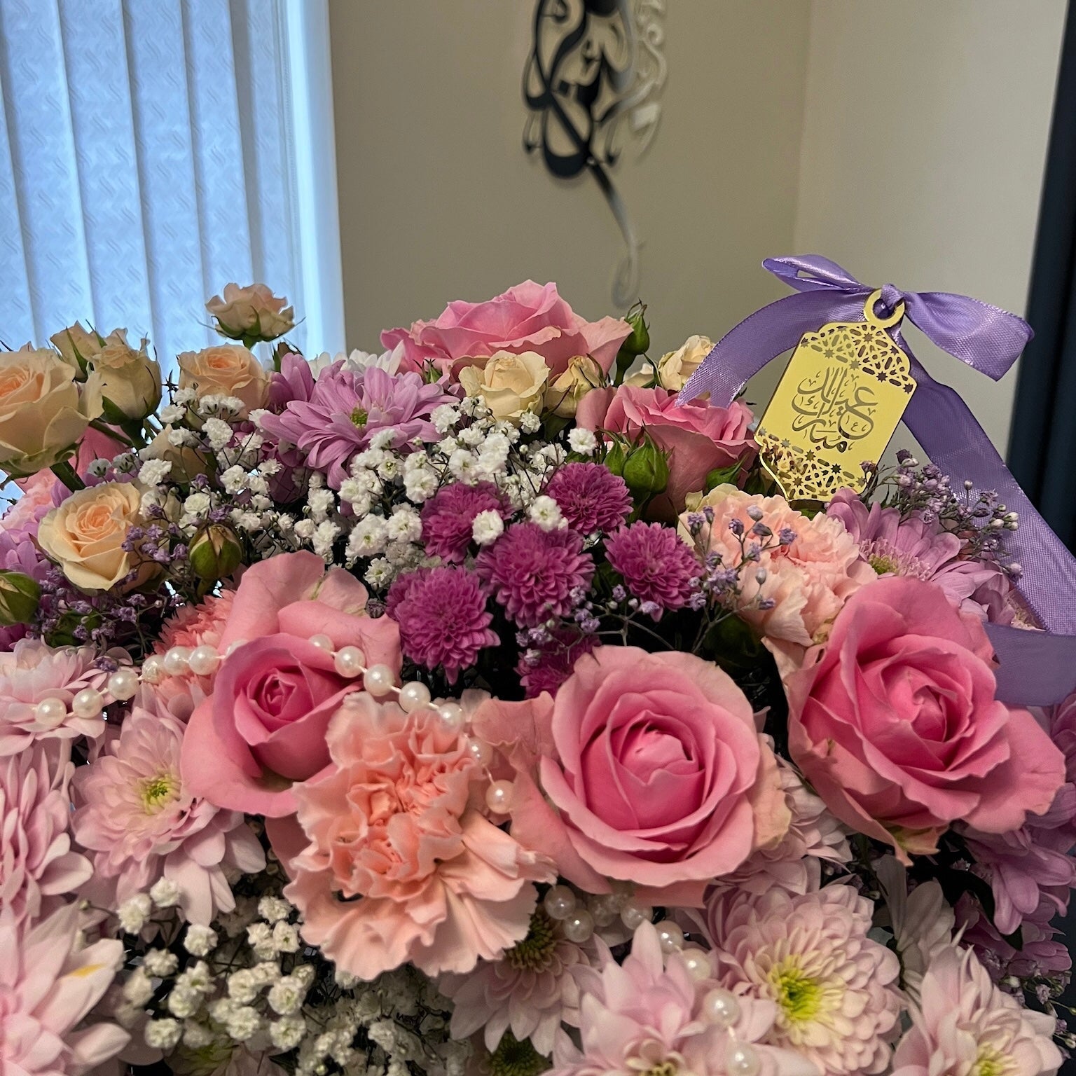 Bouquet of flowers with a purple ribbon and yellow tag in a room setting.