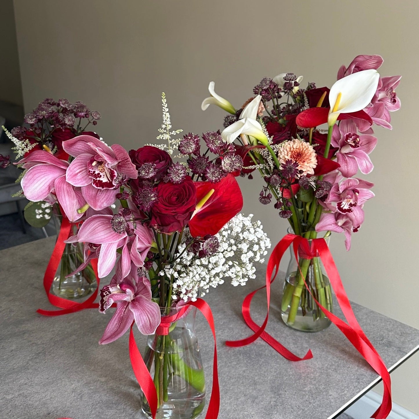 Three flower bouquets with red ribbons on a gray surface.