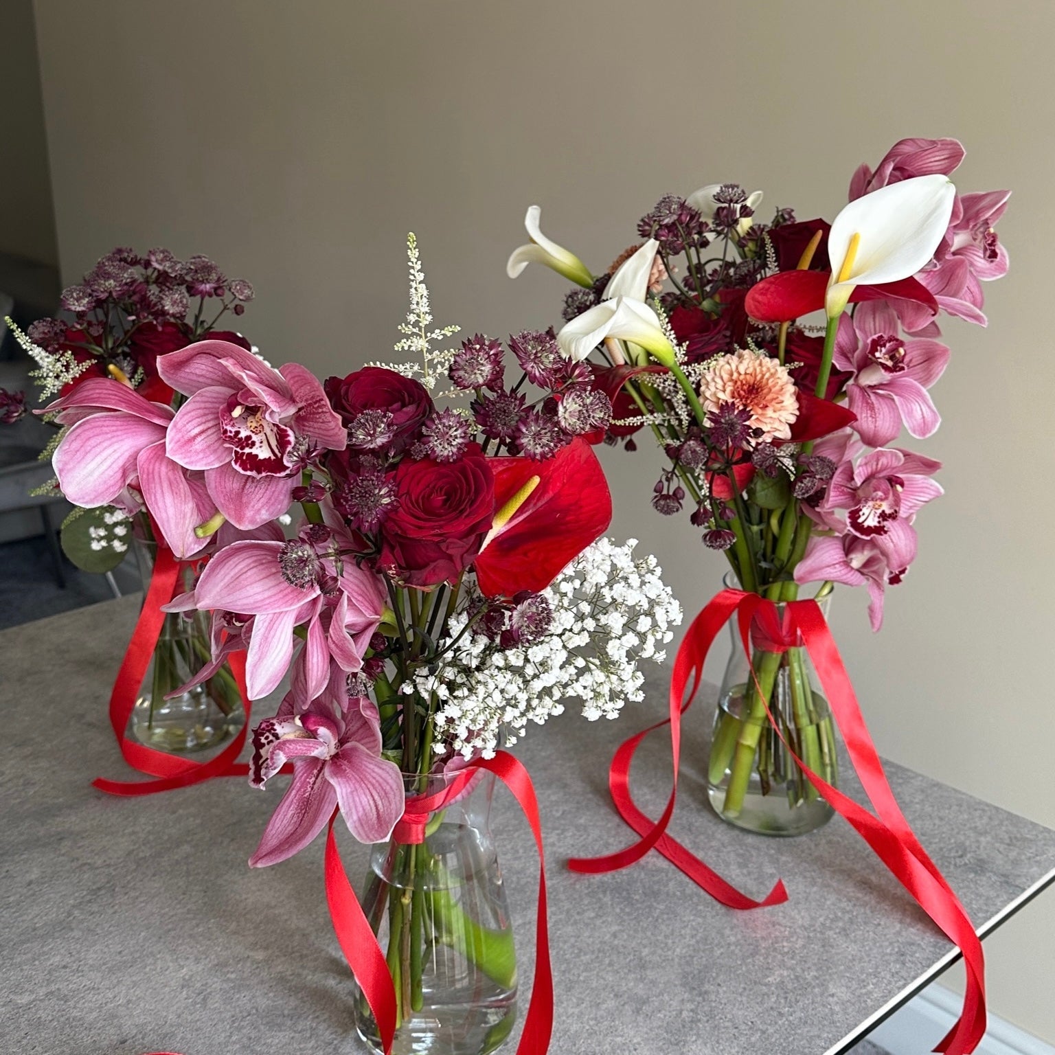 Three flower bouquets with red ribbons on a gray surface.