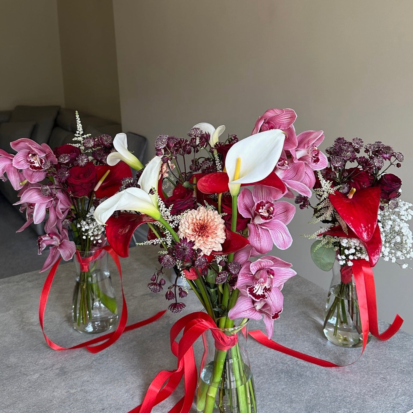 Three bouquets of flowers with red ribbons on a table against a neutral wall.