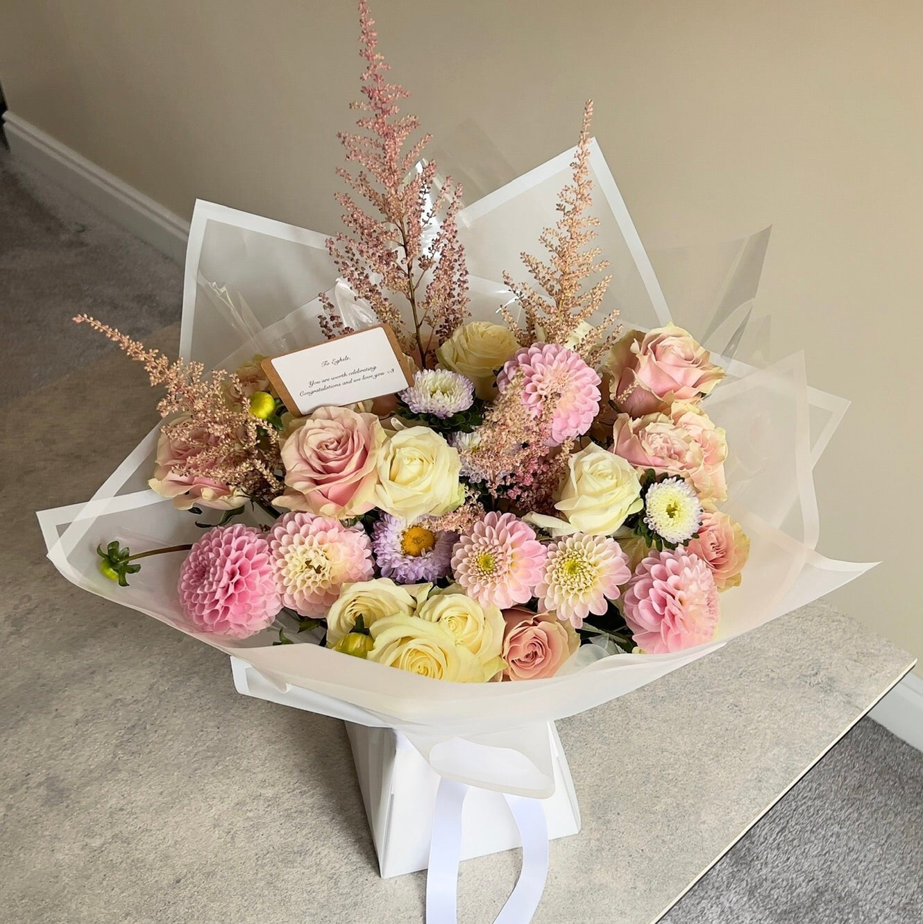 Bouquet of pastel flowers in white paper wrap on a neutral background.