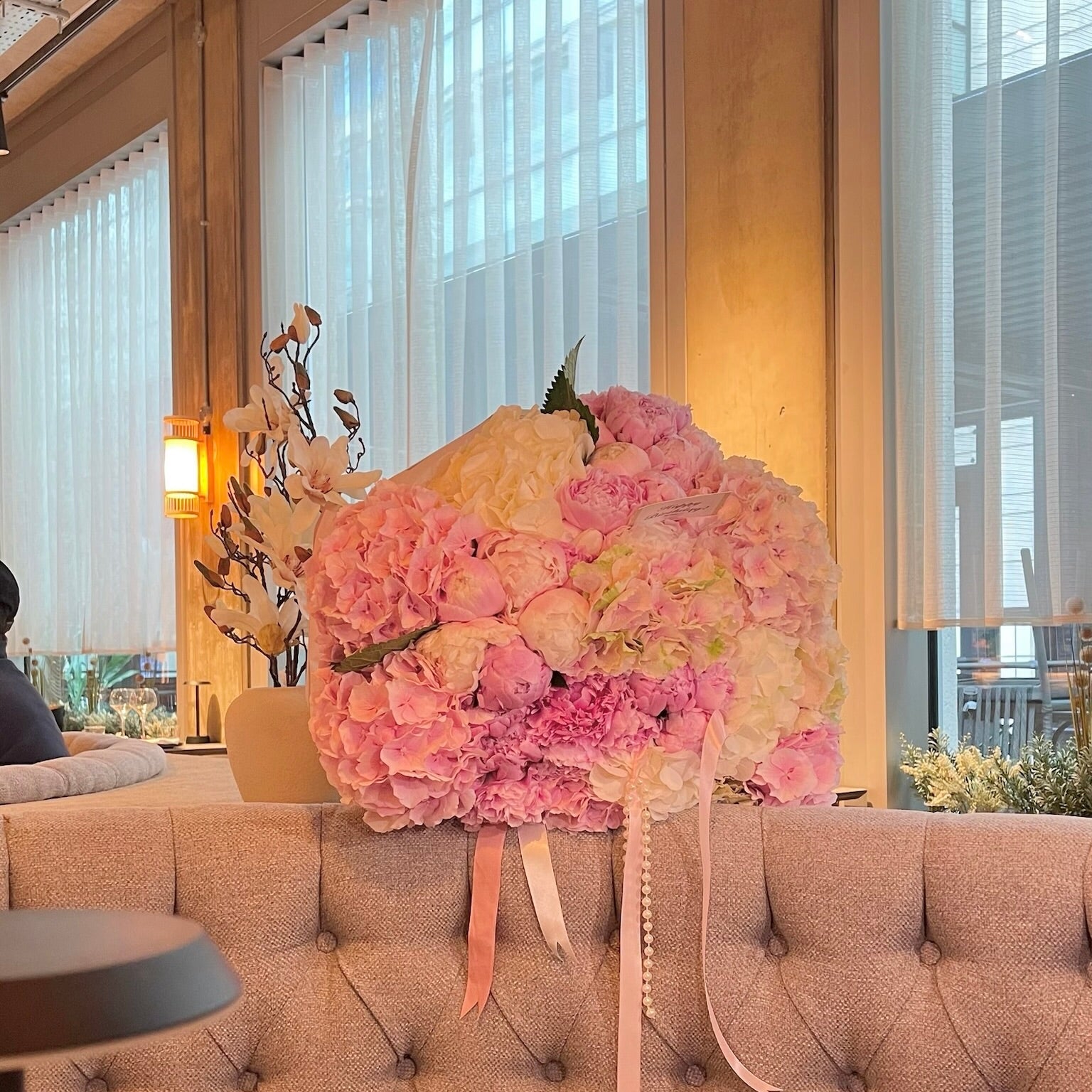Floral arrangement with hydrangeas and peonies in velour wrapping and a piece of cake on a table with a decorative box in the background.