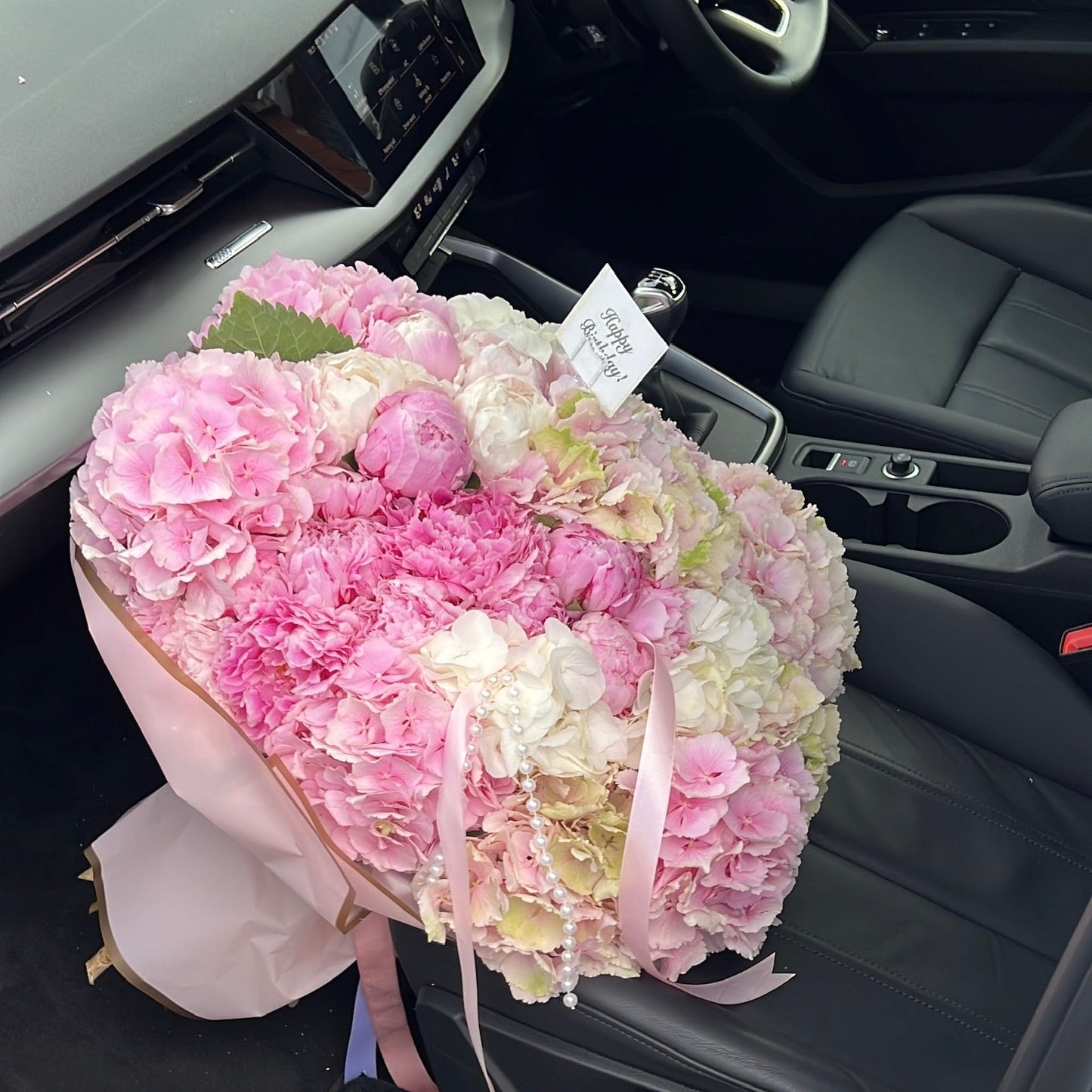 Floral arrangement with hydrangeas and peonies in velour wrapping and a piece of cake on a table with a decorative box in the background.