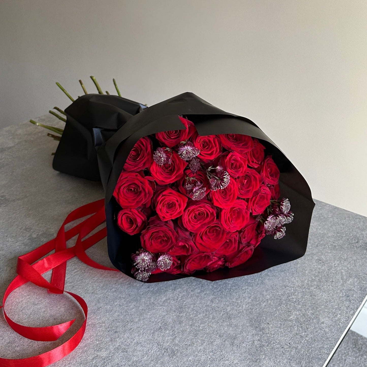 Bouquet of red roses wrapped in black paper with a red ribbon on a gray surface.