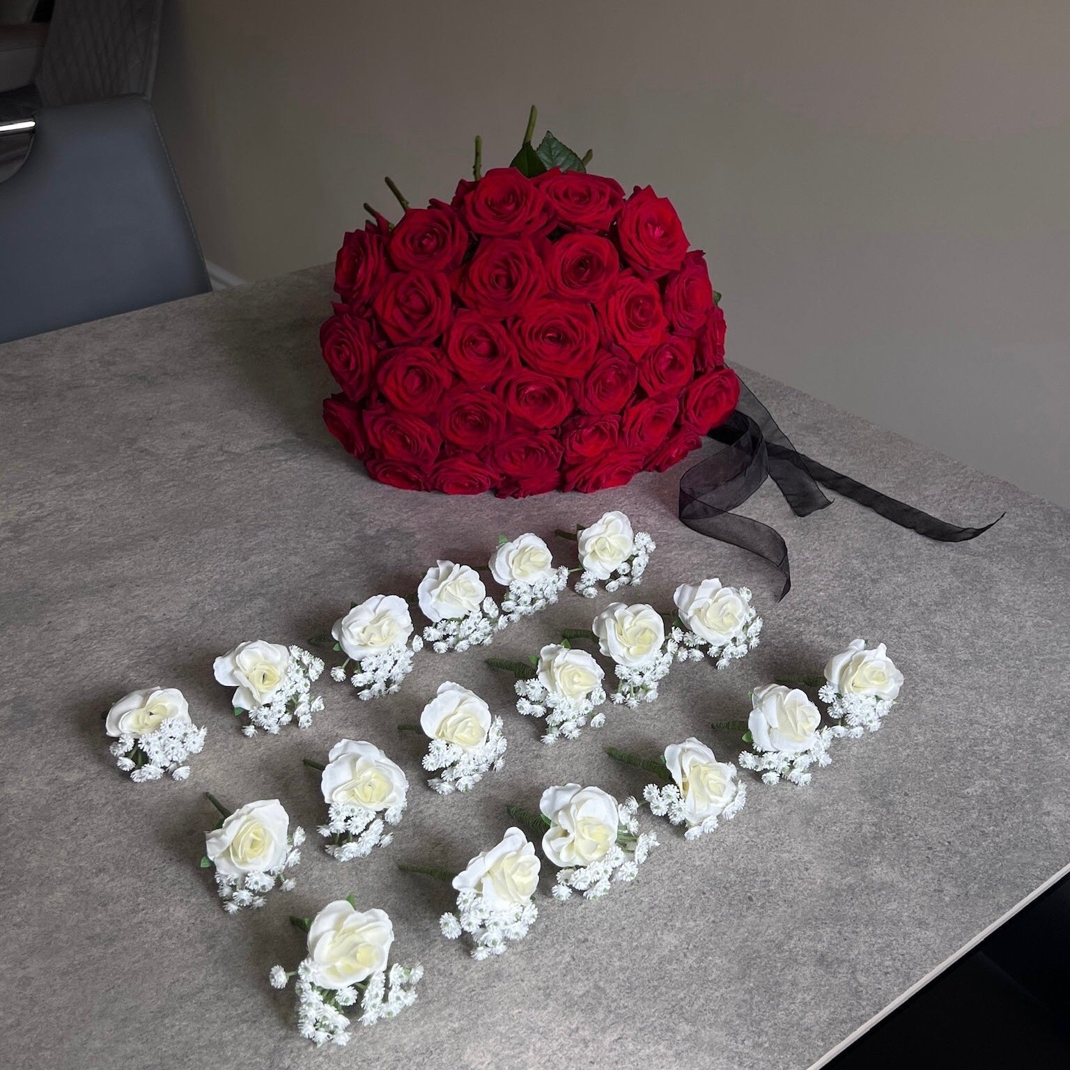 Bouquet of red roses and white floral hair accessories on a gray surface.