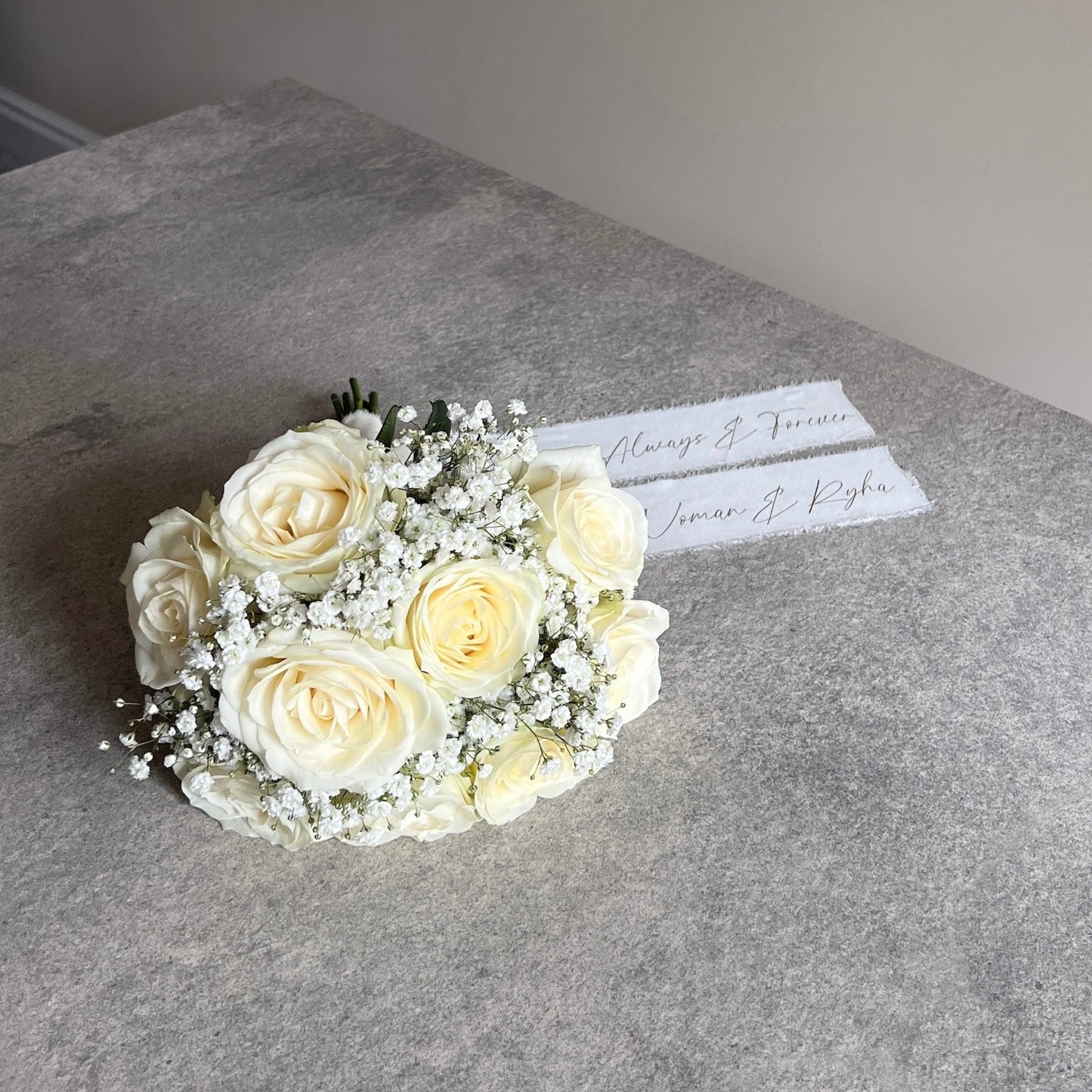 Bouquet of white roses on a gray surface with a name card.
