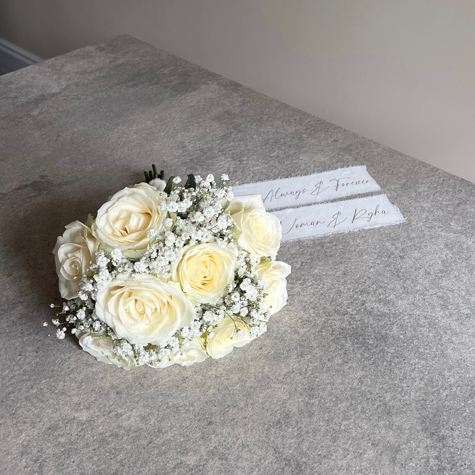 Bouquet of white roses on a gray surface with a name card.