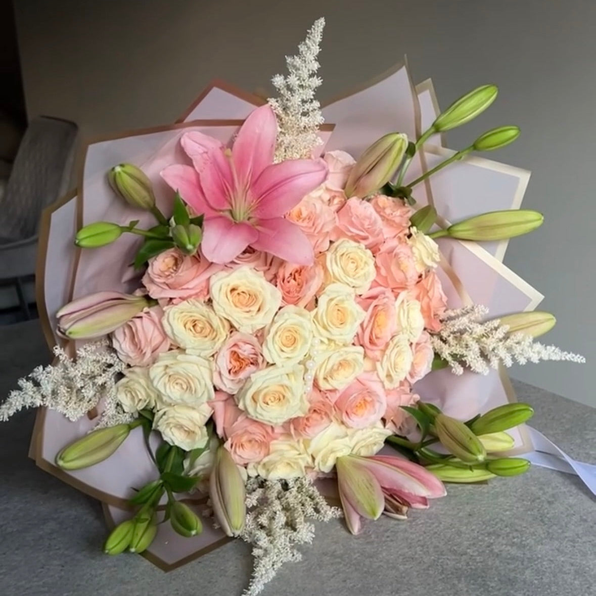 Bouquet of pink, white, and green flowers on a gray surface with stargazer lilies surrounding it. 