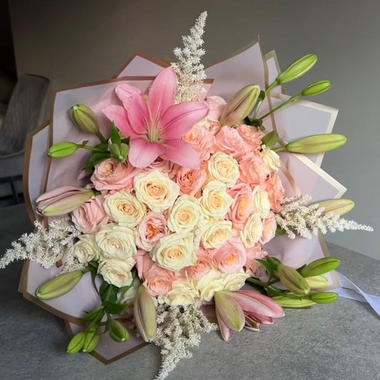 Bouquet of pink, white, and green flowers on a gray surface with stargazer lilies surrounding it. 