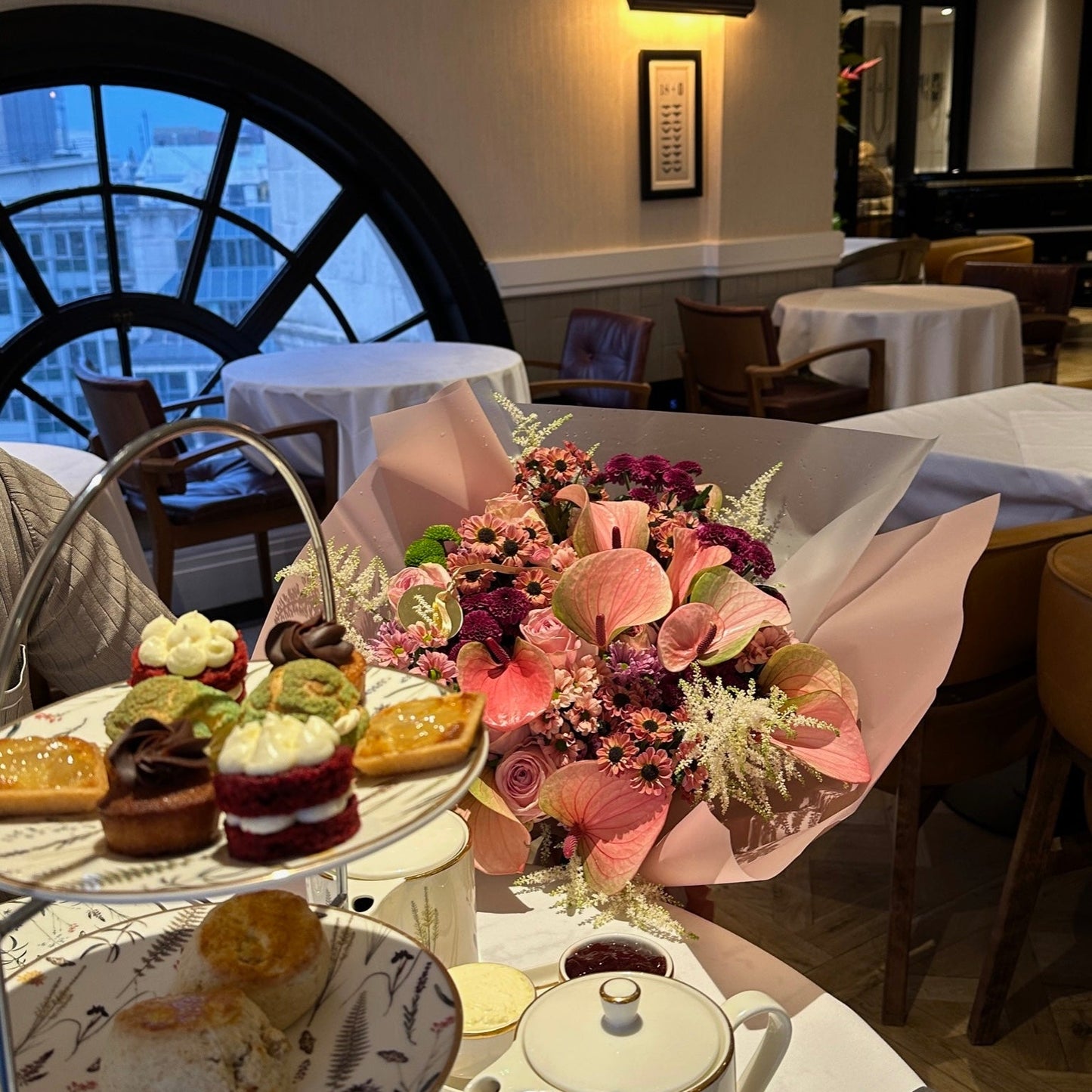 Tea set with pastries and a bouquet of flowers on a table in a restaurant setting.