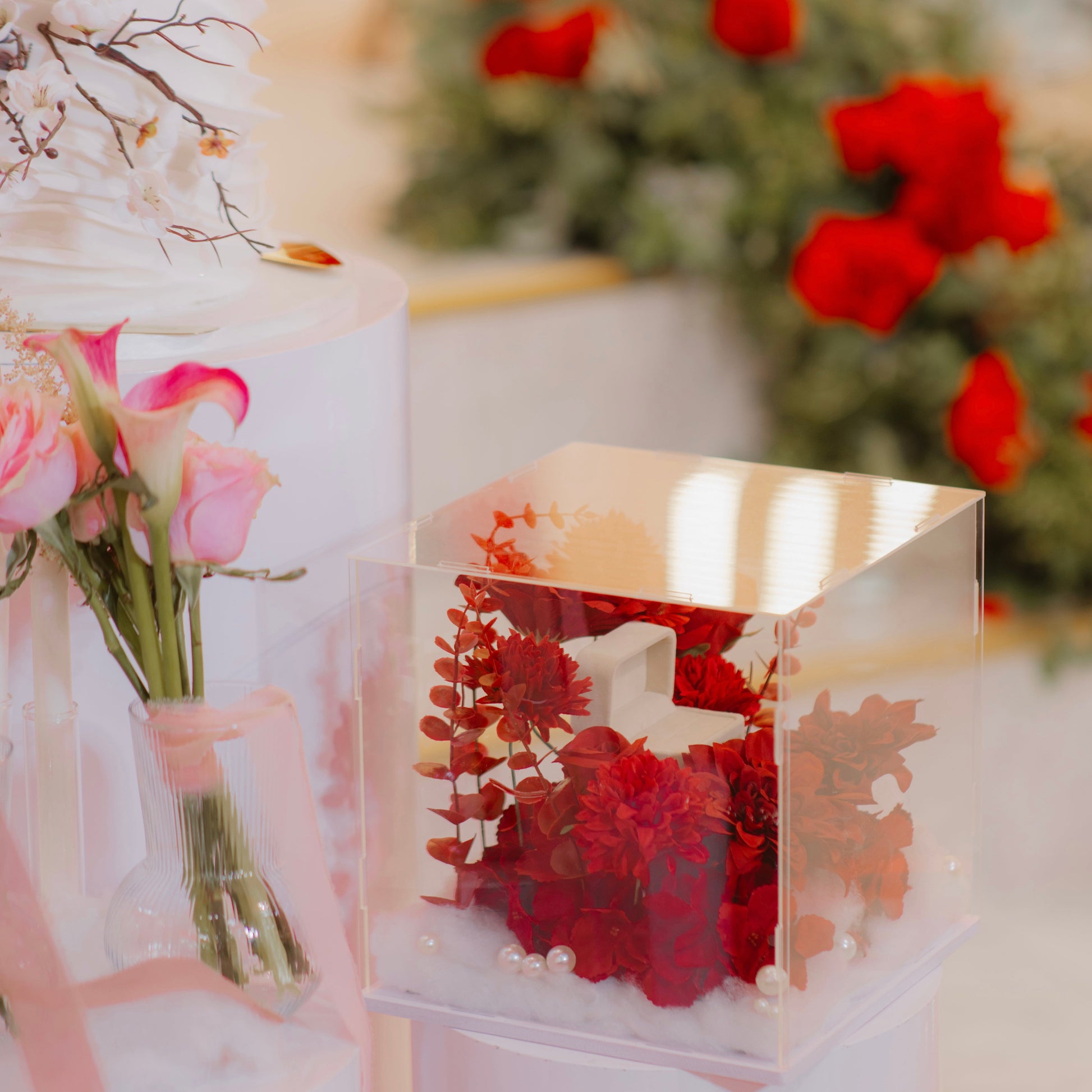 Clear box with red flowers and pearls, surrounded by pink roses and greenery, this is a ring box