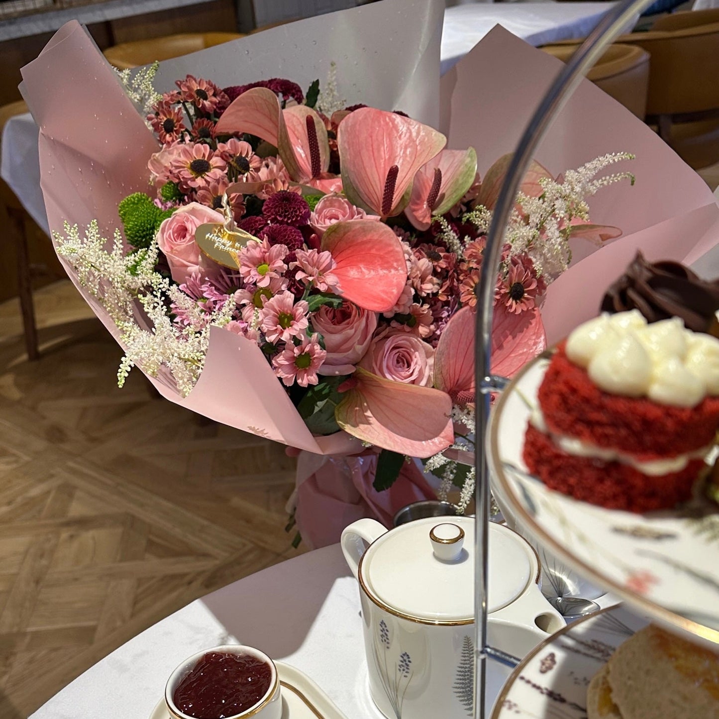 Bouquet of flowers and a red velvet cake on a tiered stand with tea set in the background.