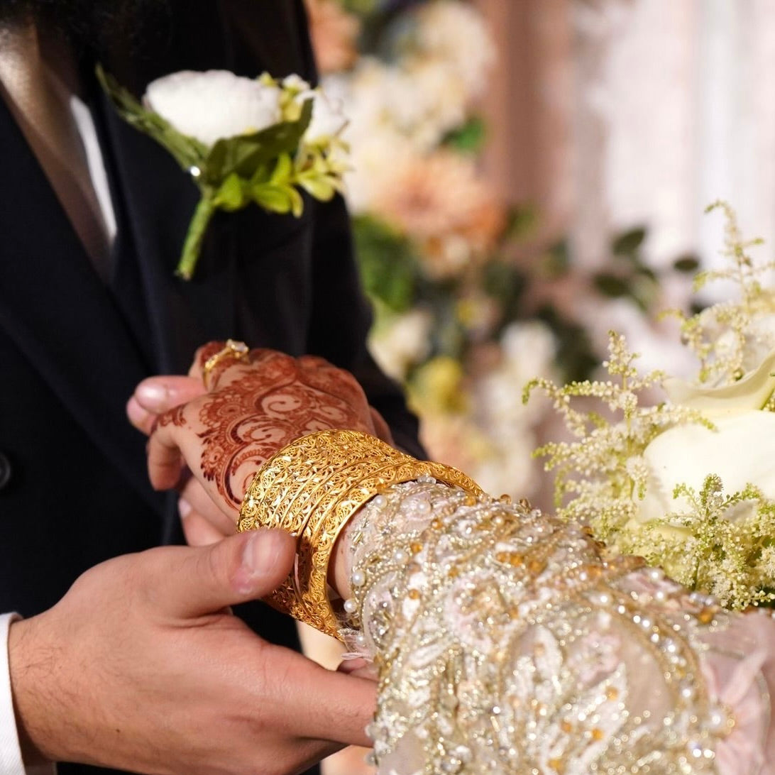 Person holding a bouquet with intricate gold design, blurred floral background