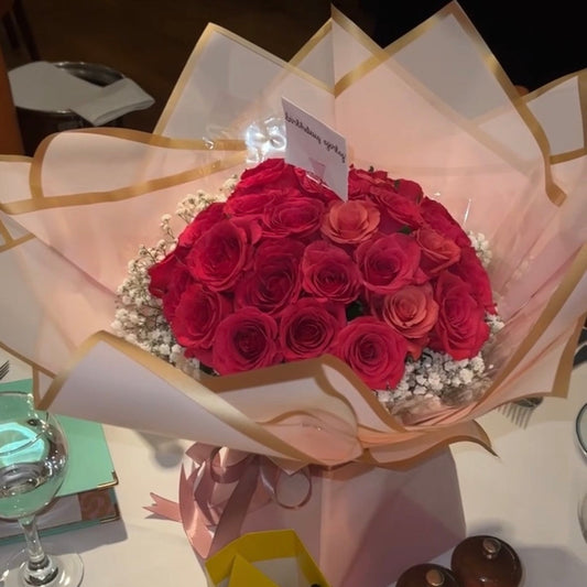 Bouquet of pink roses in a decorative wrap on a table with a glass and books.