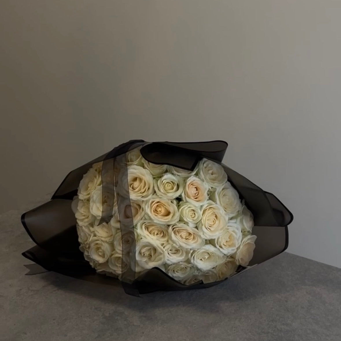 Bouquet of white roses wrapped in black paper on a neutral background