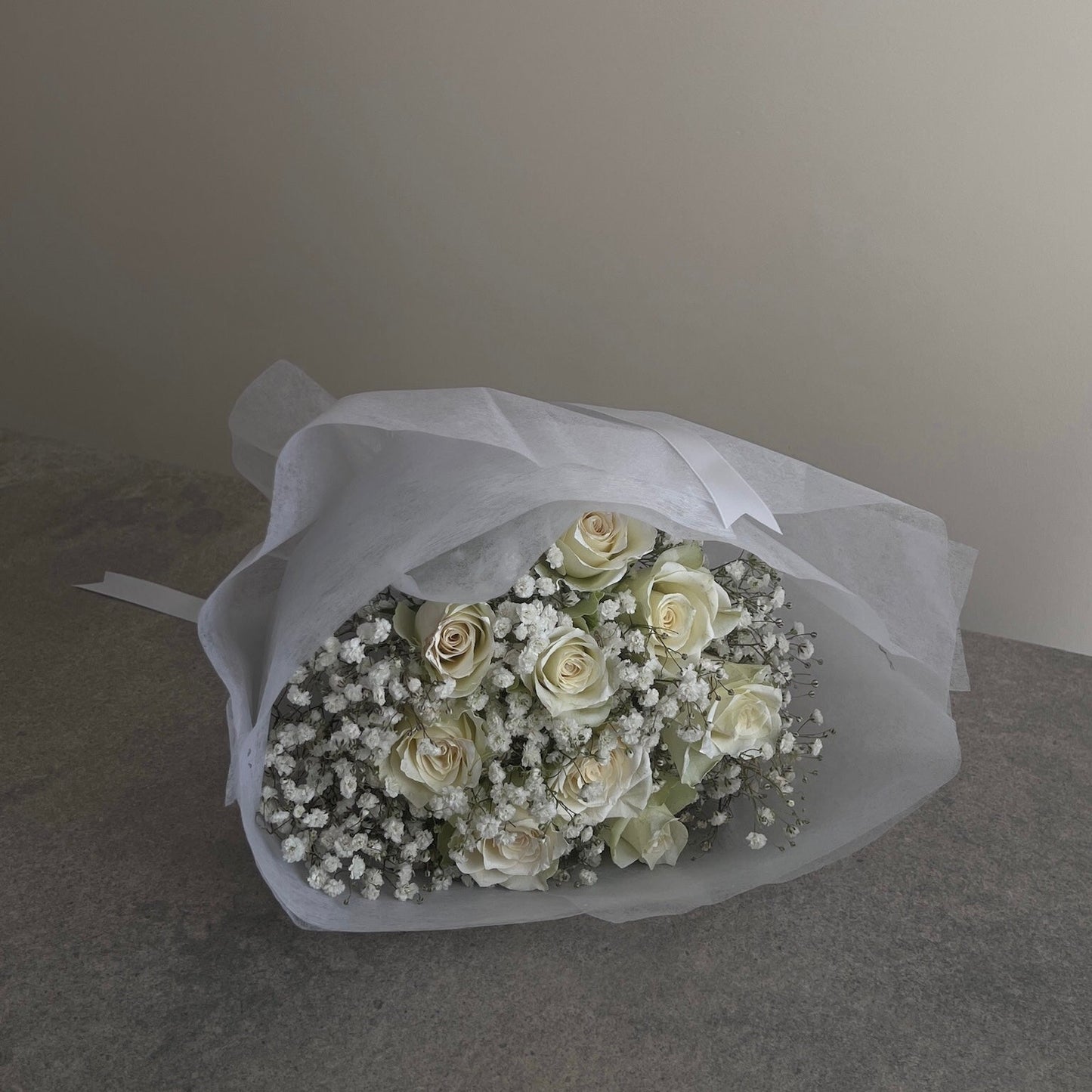 Bouquet of white roses and baby's breath wrapped in white paper on a gray surface.
