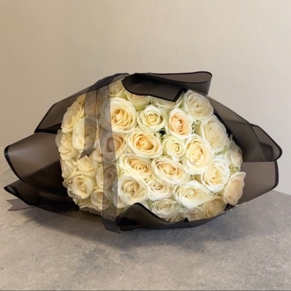 Bouquet of white roses wrapped in black paper on a neutral background