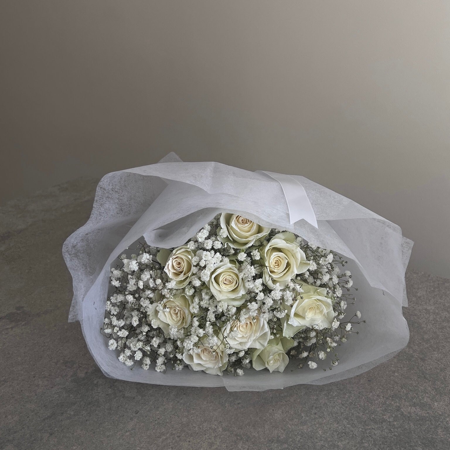 Bouquet of white flowers wrapped in white paper on a gray surface